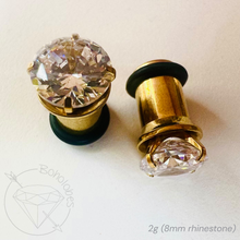 Load image into Gallery viewer, two gold-colored earring backs with large, clear gemstones attached to them.