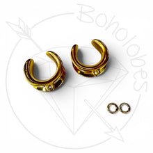 Load image into Gallery viewer, a pair of gold-colored earrings with a small gemstone, along with two smaller earring backs, all set against a white background with a stylized graphic design.