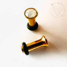 Load image into Gallery viewer, two gold-colored metal objects, one with a clear gemstone in the center, placed on a white surface.