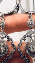 Load image into Gallery viewer, A close-up view of a person's hand wearing a pair of ornate, diamond-encrusted earrings.