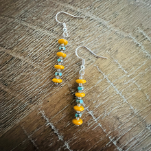 Load image into Gallery viewer, A pair of earrings with yellow beads and silver hooks, resting on a wooden surface.
