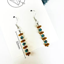 Load image into Gallery viewer, A pair of earrings with a row of small, round beads in shades of brown and blue, hanging from a hook.